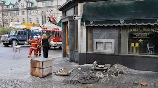 The street scene shows damage caused by an explosion in a manhole as a result of gases generated by a low-voltage arcing fault.