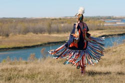 A person in American Indian clothes on empty land, beside a water body A person in American Indian clothes on empty land, beside a water body