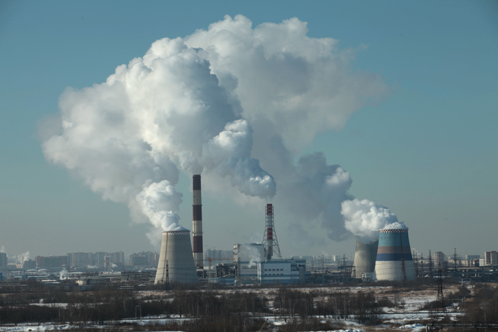 Power plants emit smoke with buildings in the background