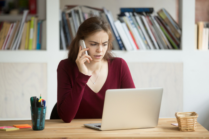 A woman looking unhappy as she speaks on the phone with a laptop open in front of her