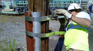 A contractor tightens metal bands used to secure a steel reinforcement to a wooden utility pole.