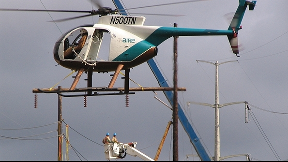 Helicopters offer air support for linemen working from a bucket truck
