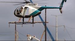Helicopters offer air support for linemen working from a bucket truck.