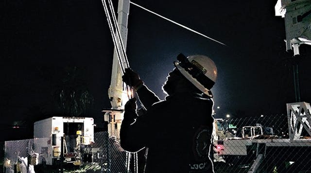 A SCE lineman is backlit by bright lights as he helps to repair a transmission line in Santa Ana, Calilfornia.