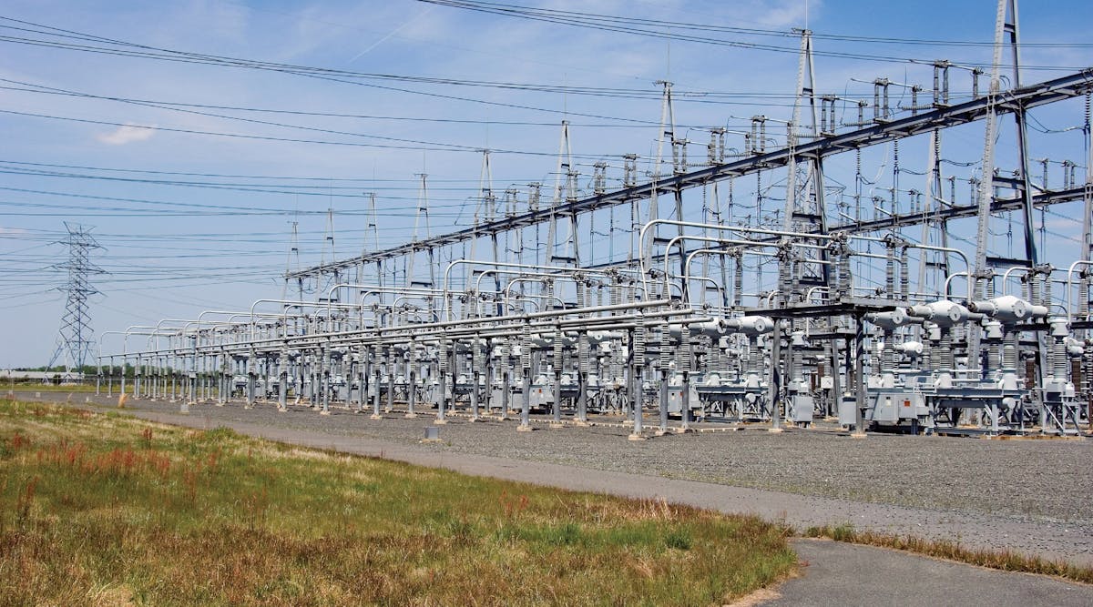 Substation with transmission tower in background. Electric distribution, transformers, switch, radiator, fuse, bus bar breaker, transmission.