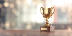 Gold award cup standing on wood surface against pale defocused background Gold award cup standing on wood surface against pale defocused background
