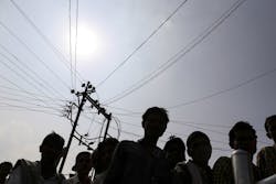 People are silhouetted as the queue under an electricity transmission pole and cables People are silhouetted as the queue under an electricity transmission pole and cables