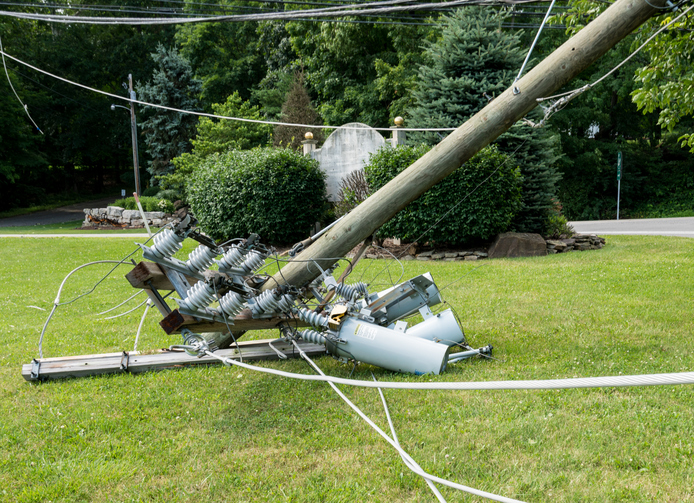 Broken snapped wooden power line post with electrical components on the ground after a storm