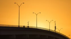 A man is walking over a bridge at sundown that spans the Indian River in Vero Beach, Florida. With the sun setting behind the bridge, the whole bridge is bathed in golden light. A man is walking over a bridge at sundown that spans the Indian River in Vero Beach, Florida. With the sun setting behind the bridge, the whole bridge is bathed in golden light.