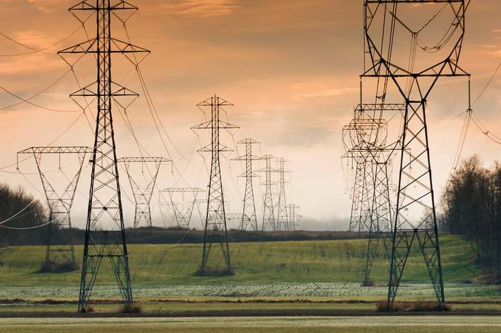 High-tension power lines run across a rural landscape at sunset