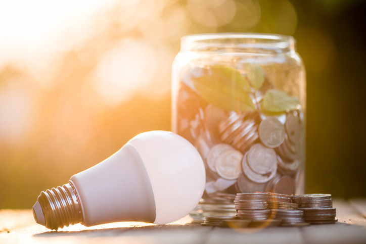 An energy-saving LED bulb next to a jar full of coins