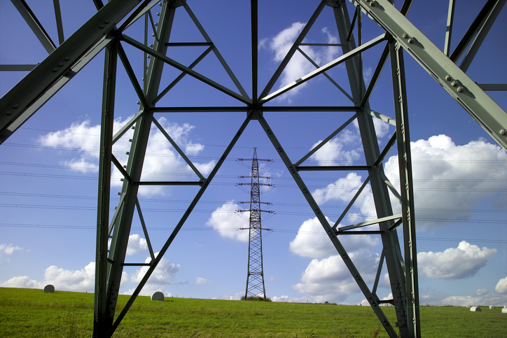 Transmission towers and power lines on a green field with blue sky and clouds in the background