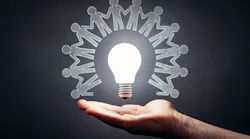 A glowing bulb surrounded by figures of people suspended on top of a hand