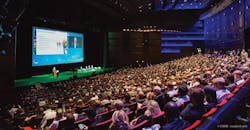 An auditorium full of people watching a presentation on stage An auditorium full of people watching a presentation on stage