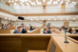 A podium microphone with blurred people in the background A podium microphone with blurred people in the background