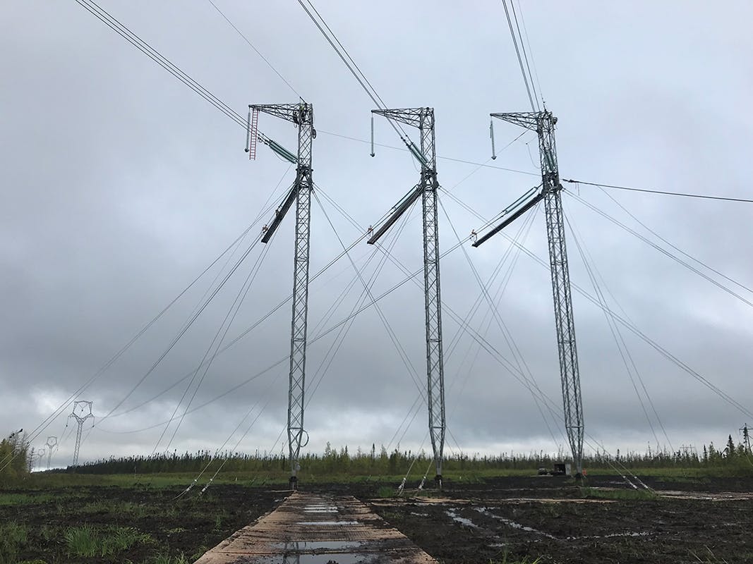 Crews are installing OPGW at a three mast guyed deadend structure in a peat bog. A helicopter was utilized to fly in the structures as well as the composite matting.