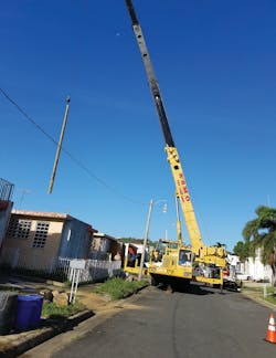A crane operator drops a pole over a house&apos;s rooftop into a backyard for installation.