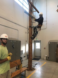 A Legacy student is shown on the pole and apprentice is shown to the right participating in inclement weather training on the Omaha Center Line Dock.