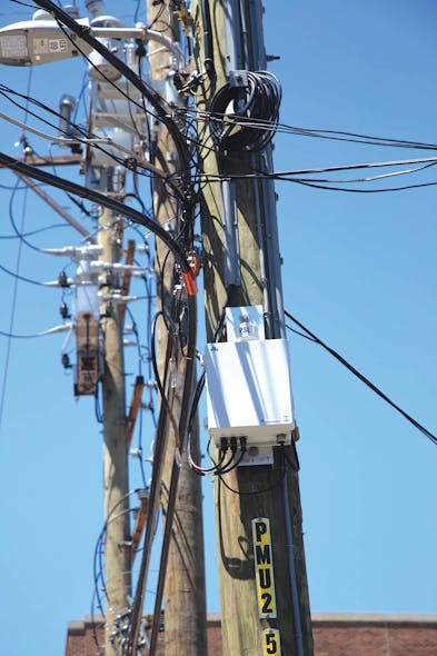 A MicroPMU telemetry cabinet is mounted on a pole nearby distribution automation devices and a capacitor bank along a busy 12-kV distribution feeder in a Chicago alley.