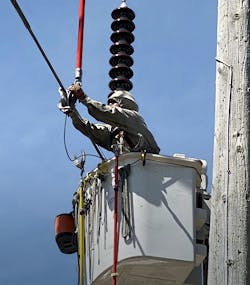 While maintaining the MAD from a wooden structure, a Three Phase Line Construction lineman in bare-hand live line suit hooks up a fiberglass strain pole to transfer an energized conductor from an old to new H-frame.