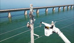 The barehand truck holds the energized 138-kV phase while members on the structure replace a polymer insulator. The barehand truck holds the energized 138-kV phase while members on the structure replace a polymer insulator.