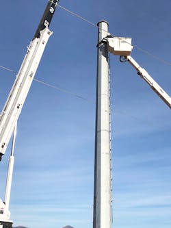 Construction crews lifted this steel H-frame tower into position with a swing cab crane and ensured its vertical placement, being careful not to hit the de-energized transmission lines.