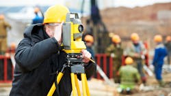 A surveyor peers through a theodolite at an outdoor construction site. Underground obstacles must be considered when burying power lines. A surveyor peers through a theodolite at an outdoor construction site. Underground obstacles must be considered when burying power lines.