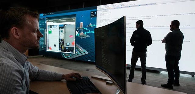 Photo of an NREL cybersecurity researcher performing work on a computer while two other researchers look at data on a large screen in the background. NREL researchers Josh Vannatta, Josh Rivera, and Shane McFly use the cyber range to visualize a real-time cyberattack.