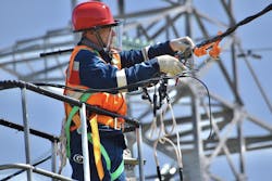 A power engineer in a car lift cradle measures the voltage after a detected short circuit on a power line using special tools. A power engineer in a car lift cradle measures the voltage after a detected short circuit on a power line using special tools.
