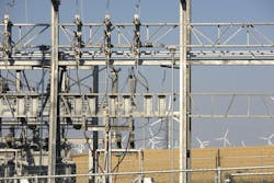 Distribution equipment frames a distant wind farm. Development of renewable energy projects is one drivers of demand for new transformers. Distribution equipment frames a distant wind farm. Development of renewable energy projects is one drivers of demand for new transformers.