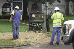Two line workers with their backs to the camera work on a electrical power transformer in a suburban neighborhood Two line workers with their backs to the camera work on a electrical power transformer in a suburban neighborhood