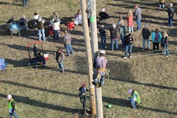 A lineworker is shown in action during an event while spectators watch another event going on simultaneously. A lineworker is shown in action during an event while spectators watch another event going on simultaneously.