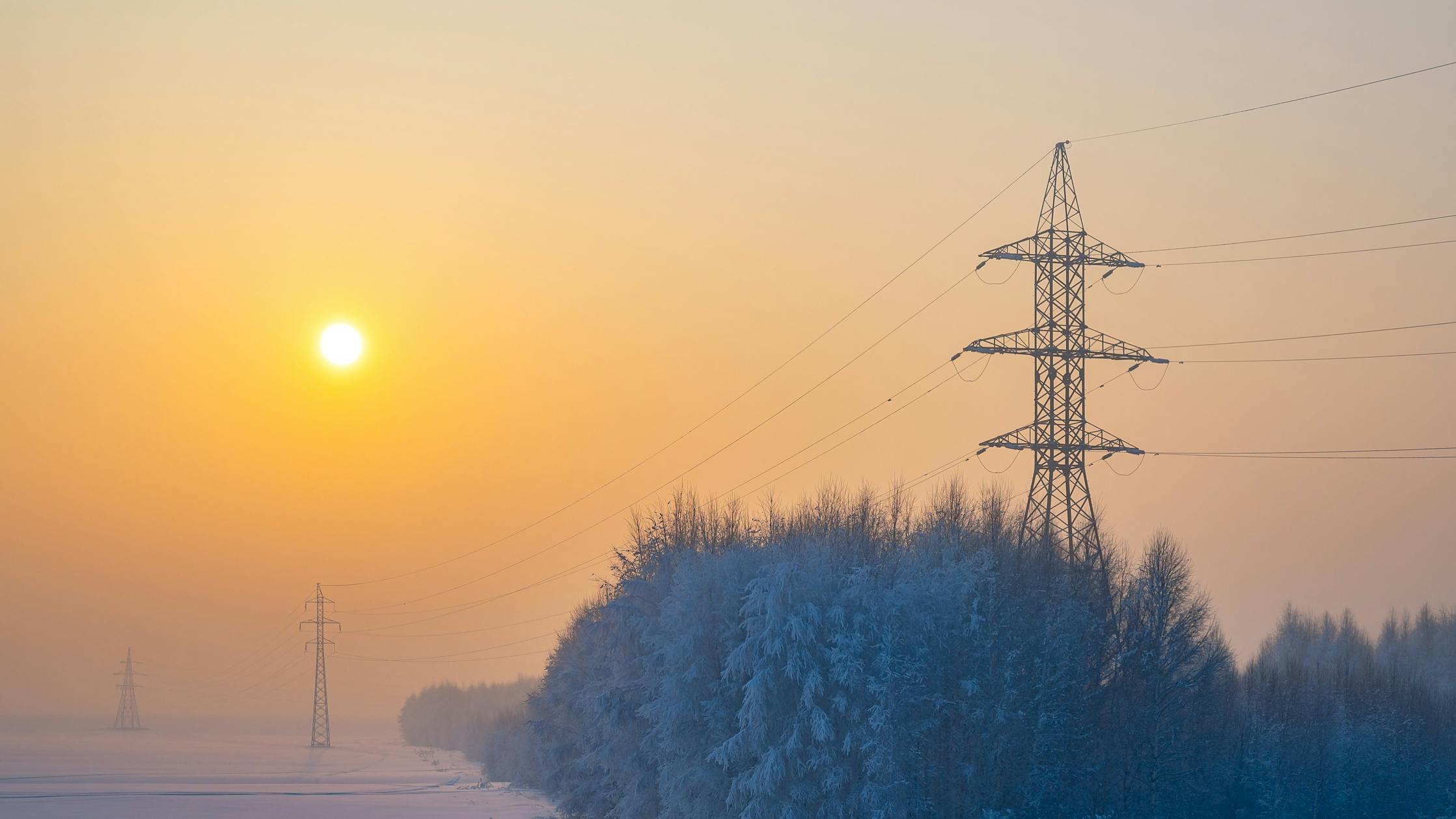 Winter morning landscape of snow covered nature, trees and large poles of high voltage power transmission lines