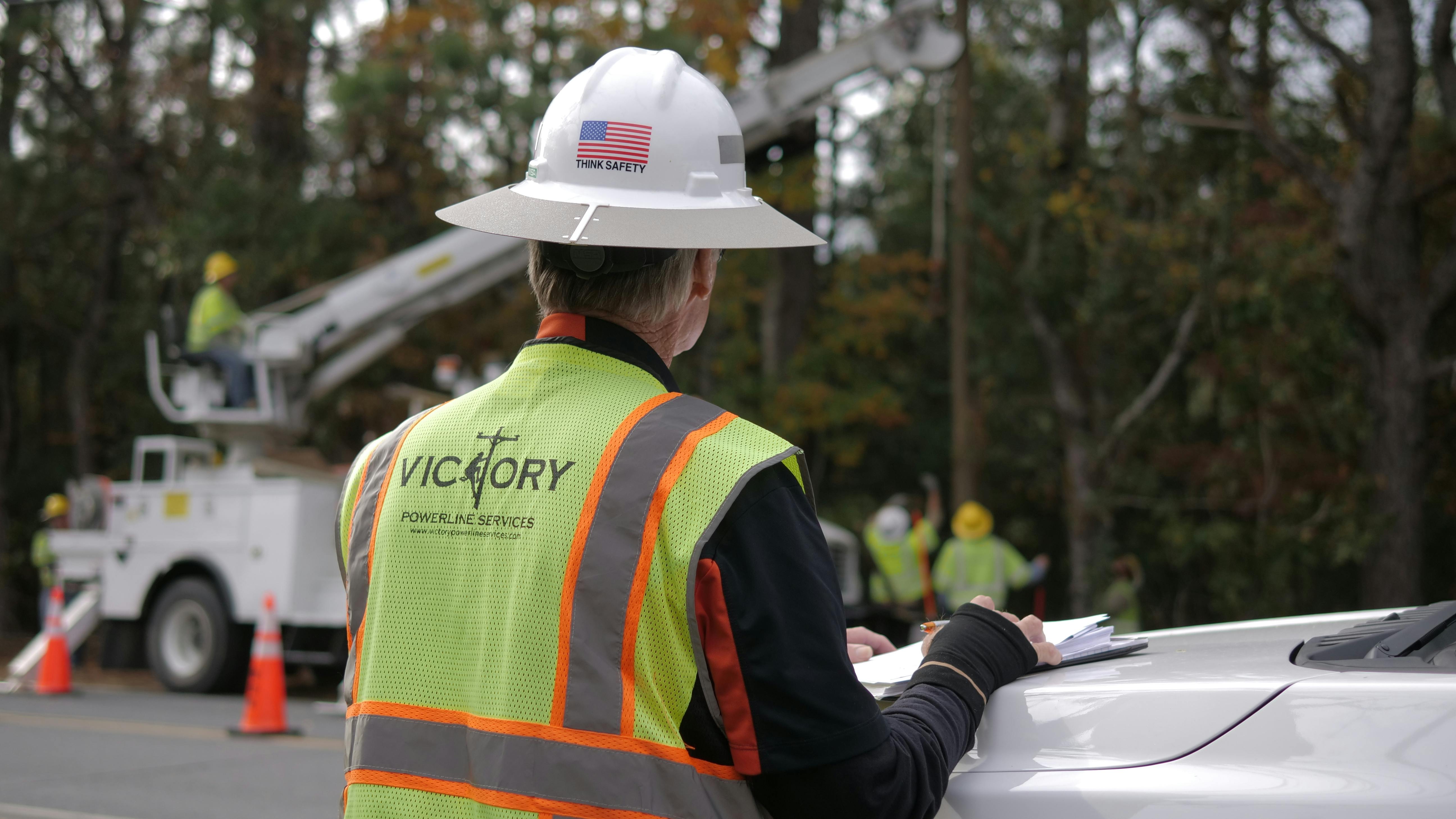 A safety professional monitors crews setting a pole