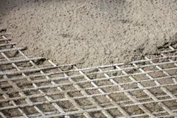 Wet concrete being poured over the steel reinforcement grid.